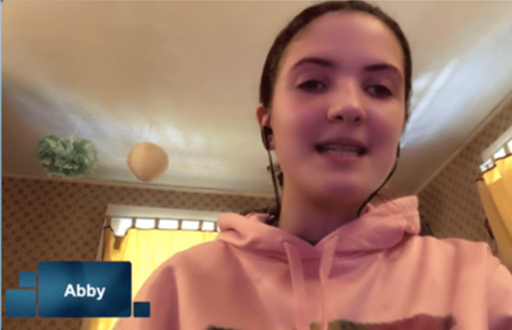 Abby smiling, wearing earbuds, and talking. 